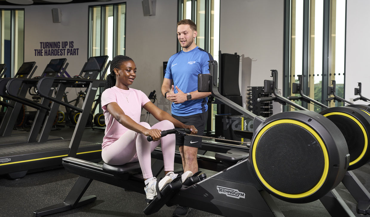 student using rowing machine with personal trainer